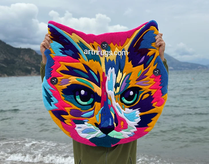 Close-up of bright multicolor impressionistic cat face rug by the water's edge