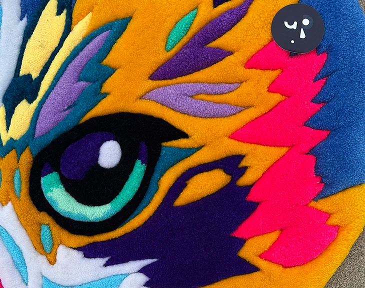 Artisan displaying vivid multicolor cat portrait rug on coastal beach