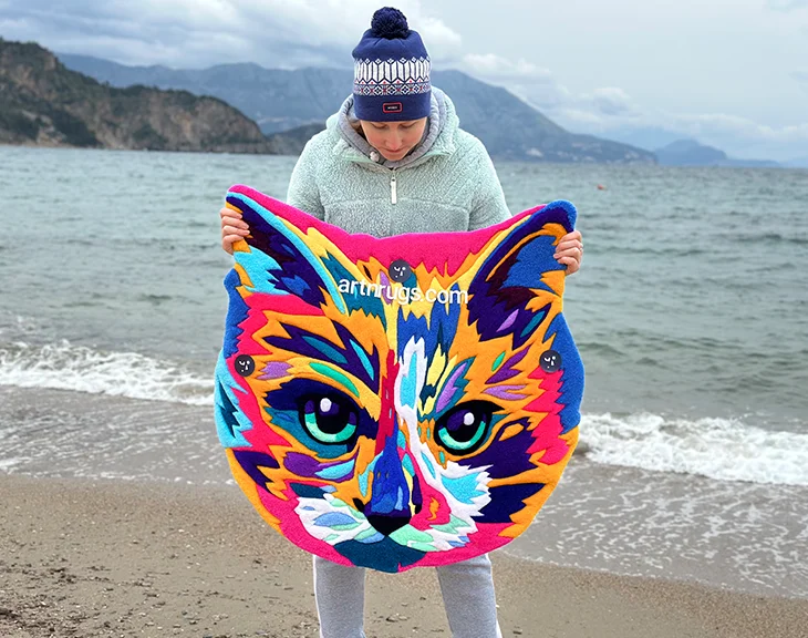 Angled view of bright multicolor cat face rug laid on sandy surface
