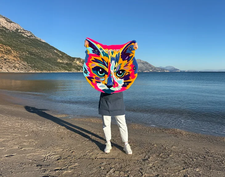 Artisan showcasing vivid multicolor cat face rug at the seaside in sunlight