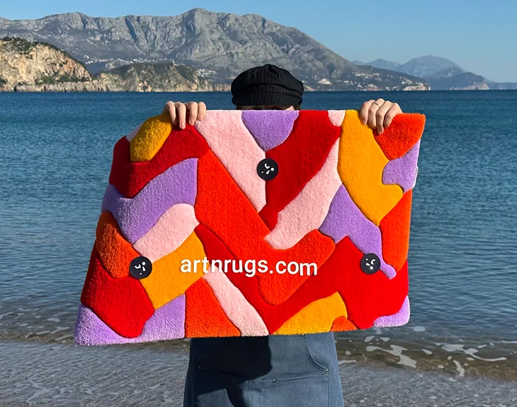 Personne tenant le Tapis Parquet Rouge et Orange devant un paysage côtier, mettant en valeur ses couleurs vives